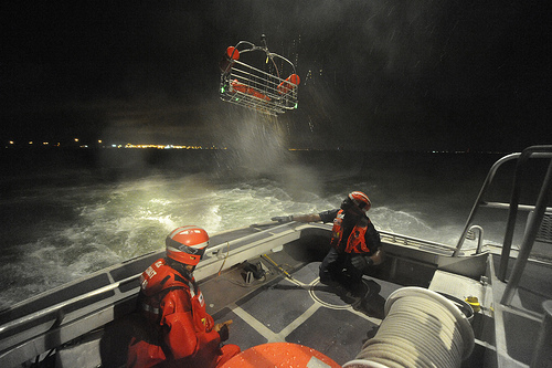 Two crewmembers from Coast Guard Station Portsmouth, Va., ensure the basket is clear of the vessel as it's being hoisted by an MH-60 Jayhawk helicopter crew from Coast Guard Air Station Elizabeth City, N.C. for training, Monday, July 30, 2012. 