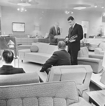 A black and white photo with 4 men dressed in suits standing in a furniture market,